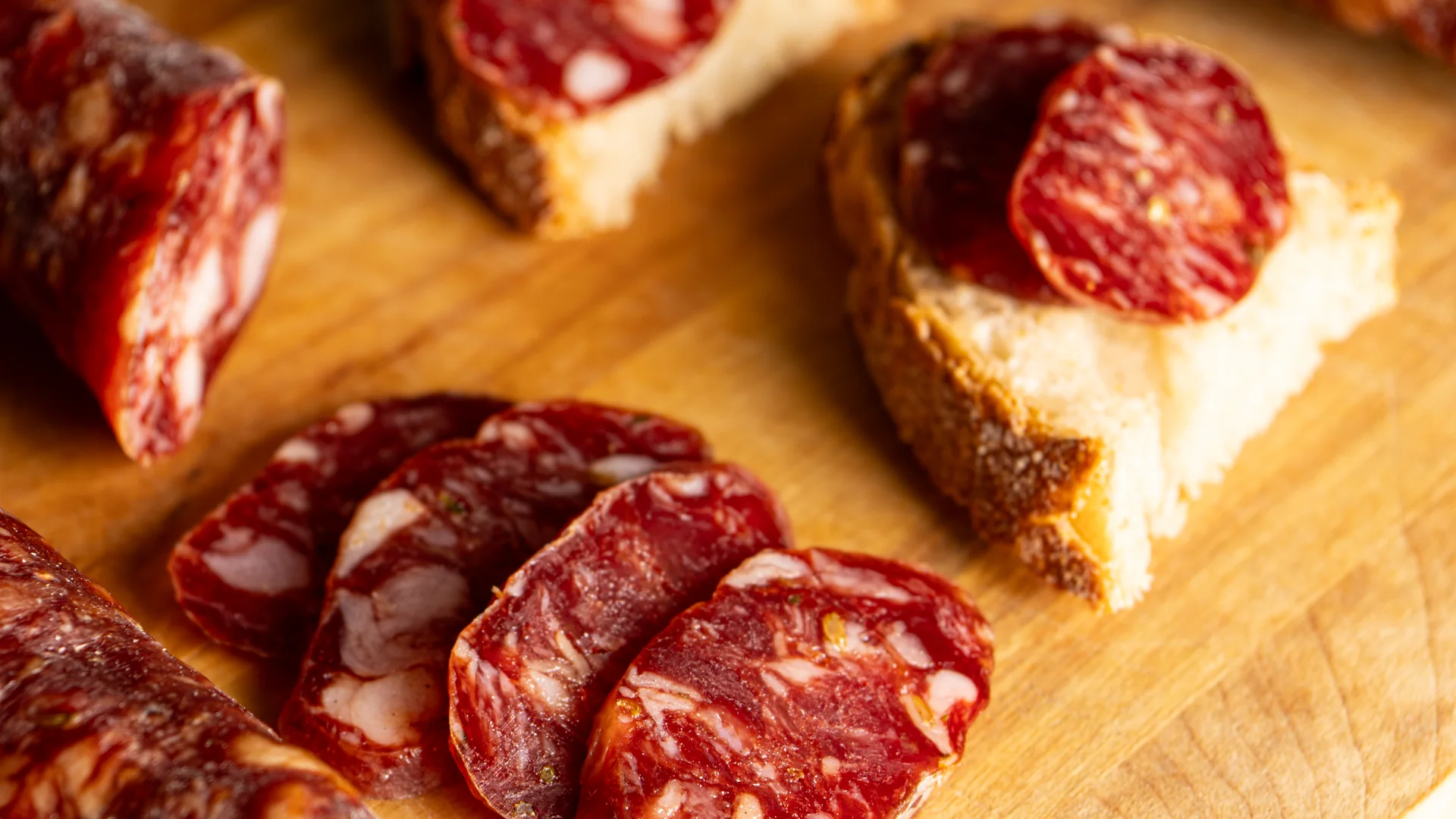 Fette di lucanica e pane su un tagliere in legno.