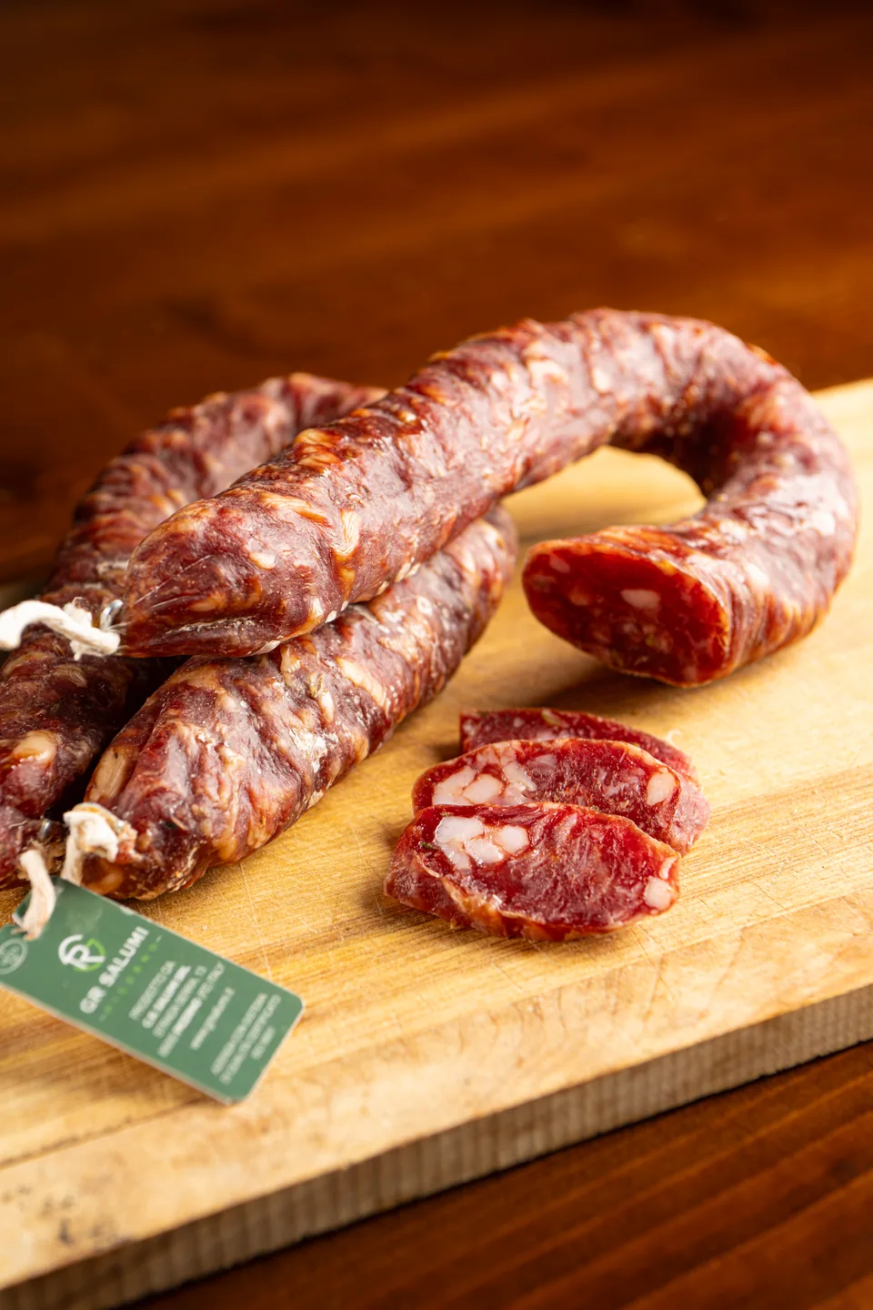 Lucanica intera e affettata su un tagliere in legno, con cartellino G.R. Salumi.
