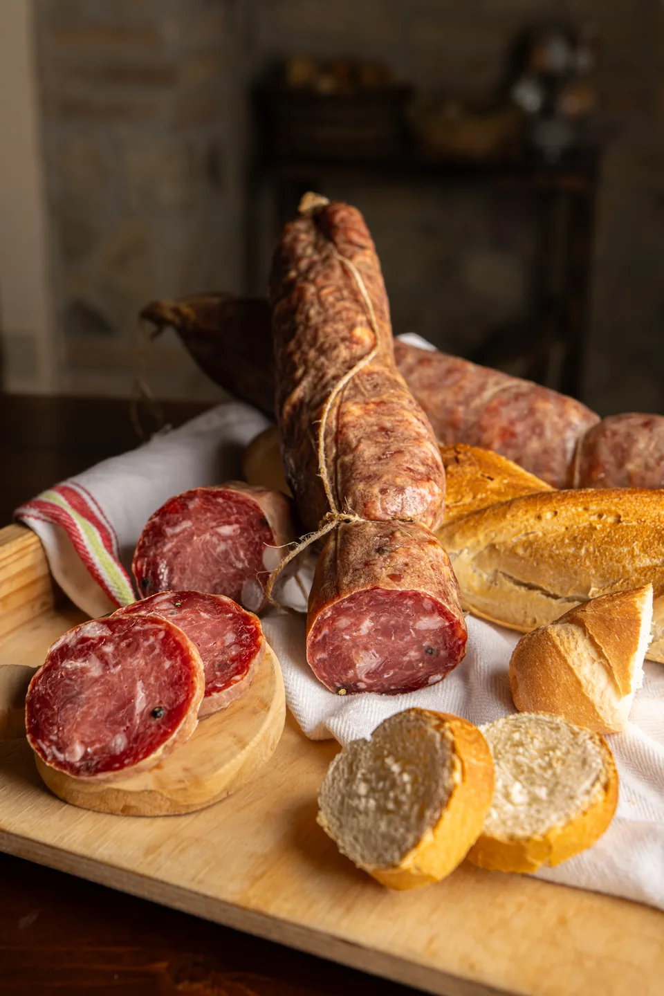 Salame intero e affettato con pane su un tagliere in legno.